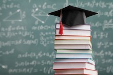 stack of books with graduation cap on top in front of whiteboard.